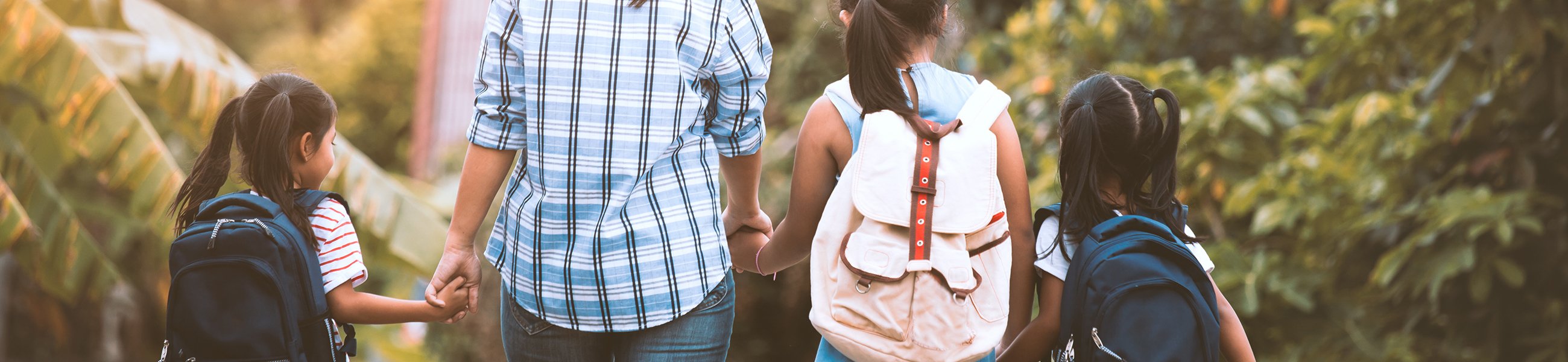 an adult walking and holding hands with 3 younger children wearing backpacks